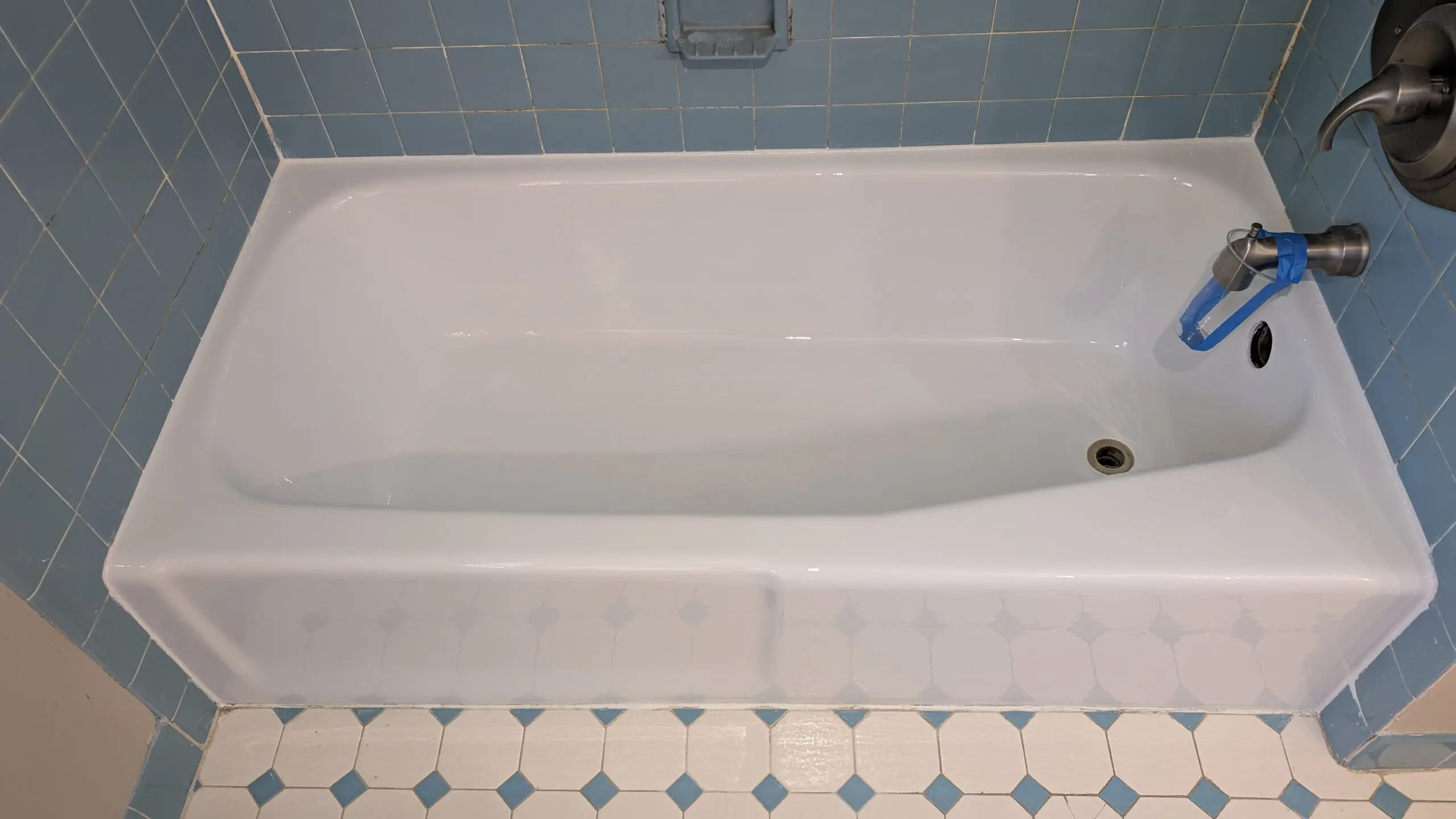 Refinished white bathtub surrounded by blue tile in a bathroom.
